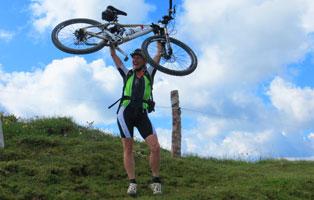 Mountainbikefahrtechniken für Frauen Frau hält Mounatinbike in die Höhe